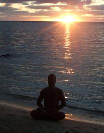 man meditating at beach at sunset